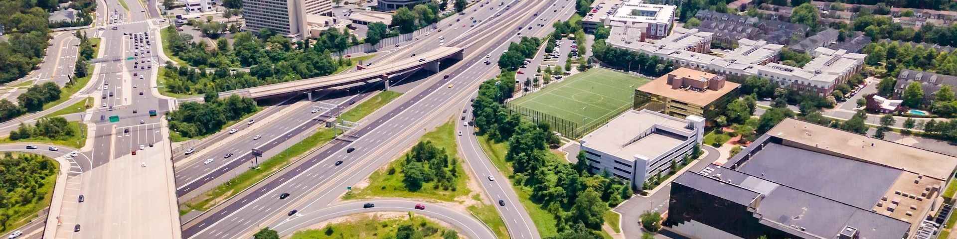 Eine mehrspurige Autobahnkreuzung mit angrenzender Stadtentwicklung und Grünflächen.