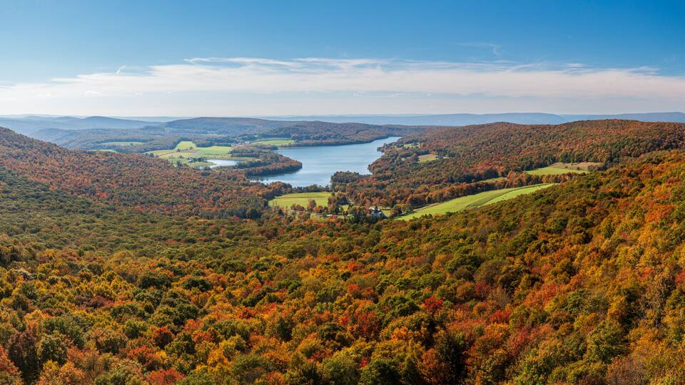 A valley with a river, surrounded by autumn-colored trees and distant mountains.