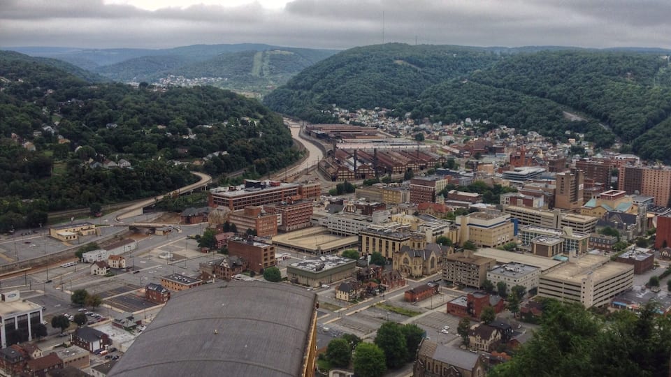 A cityscape with a river, surrounded by hills and a cloudy sky.