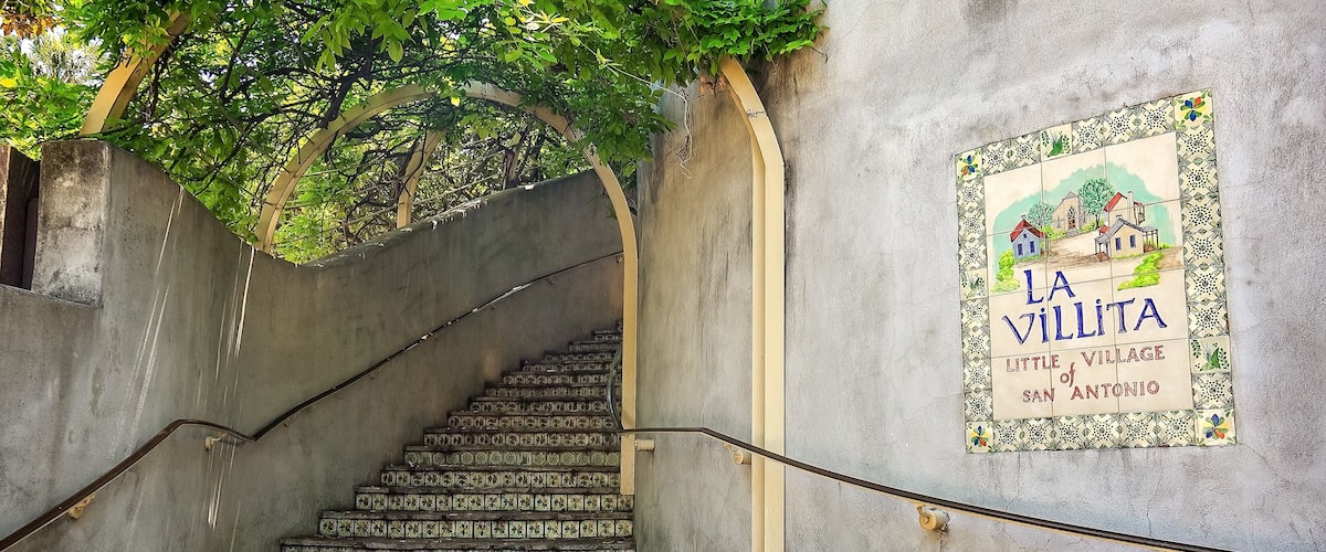 A staircase with colorful tiles leading up to a wall with a sign reading "La Villita, Little Village of San Antonio".