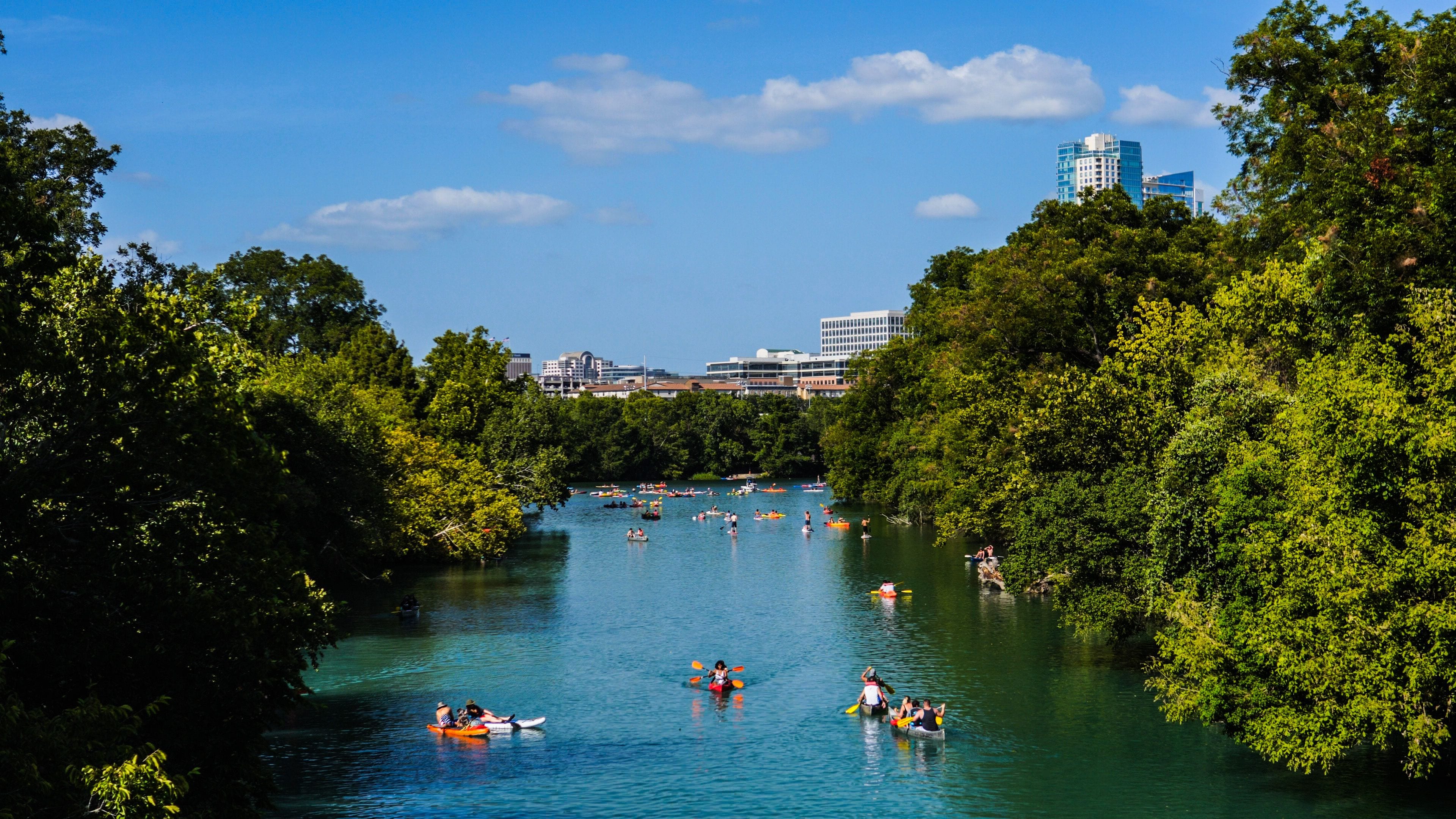 A river surrounded by dense green trees, with people kayaking and canoeing.