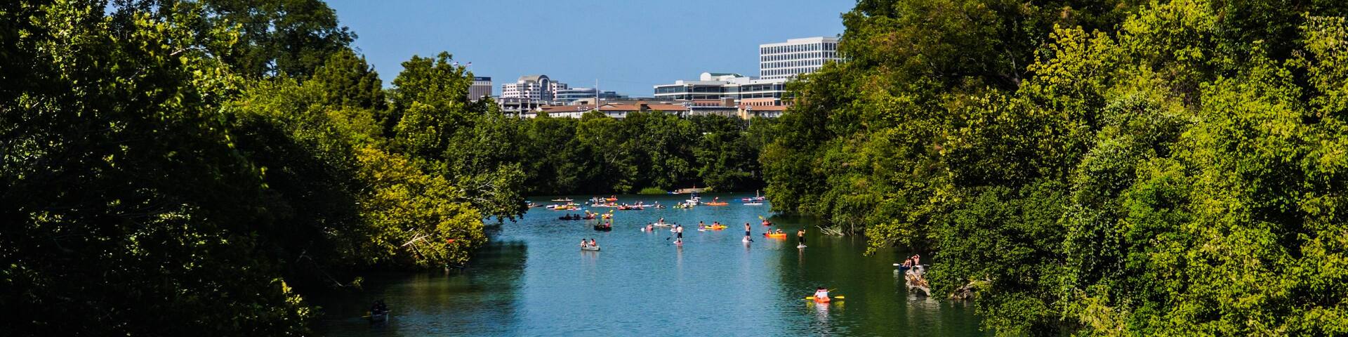 A river surrounded by dense green trees, with people kayaking and canoeing.