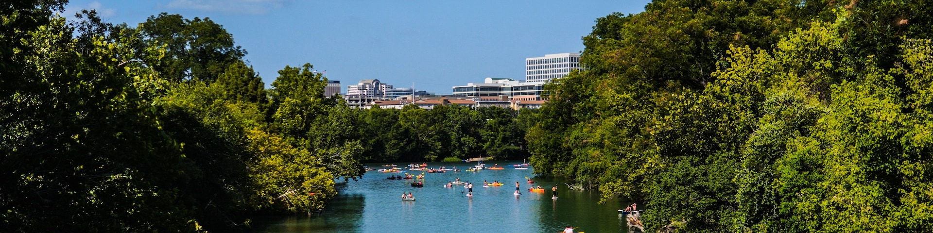 A river surrounded by dense green trees, with people kayaking and canoeing.