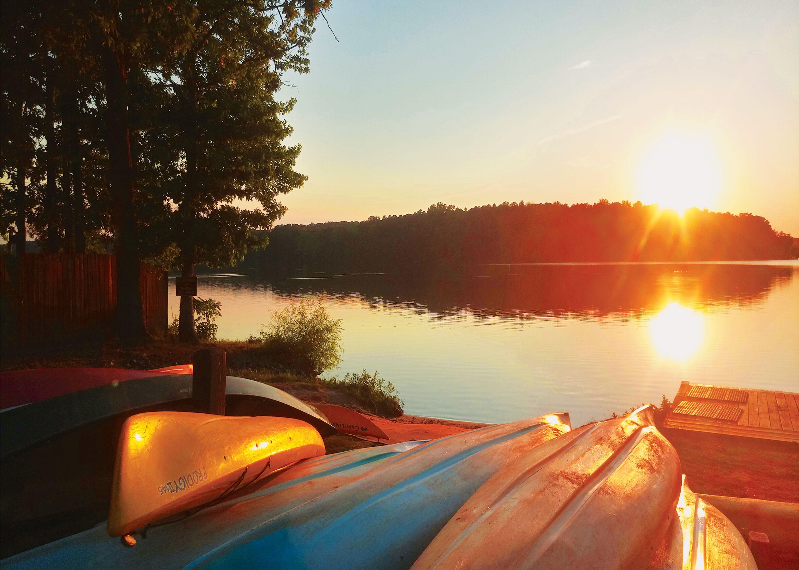A calm lake at sunset with kayaks and a dock.