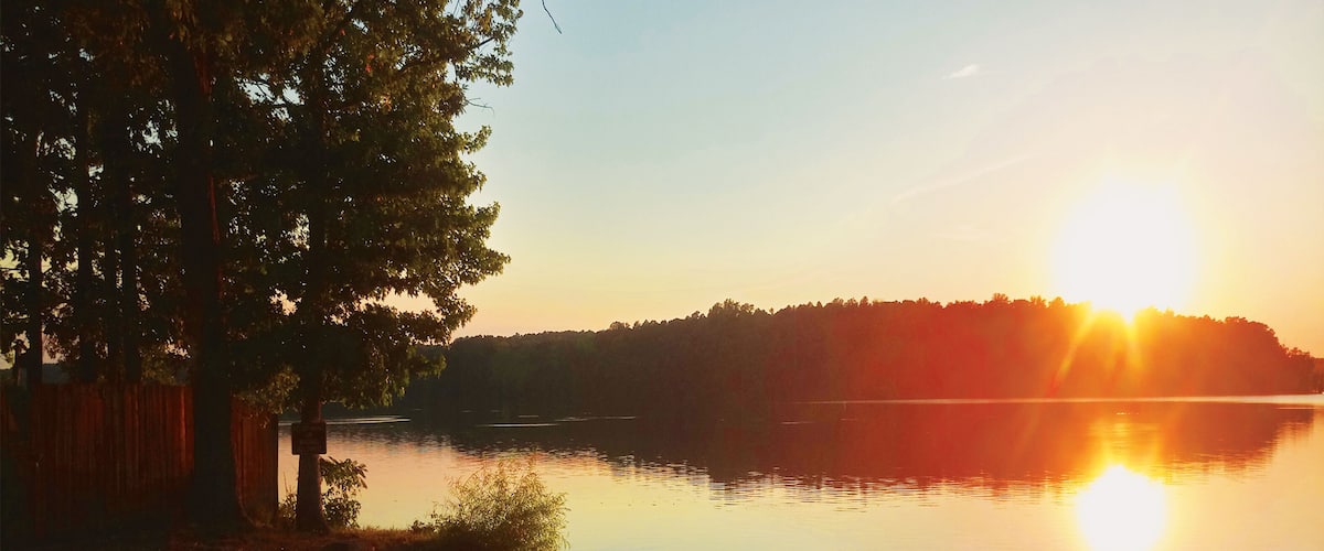 A calm lake at sunset with kayaks and a dock.