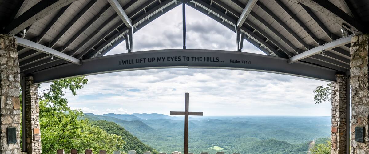 A cross in a stone structure with a view of a mountainous landscape.