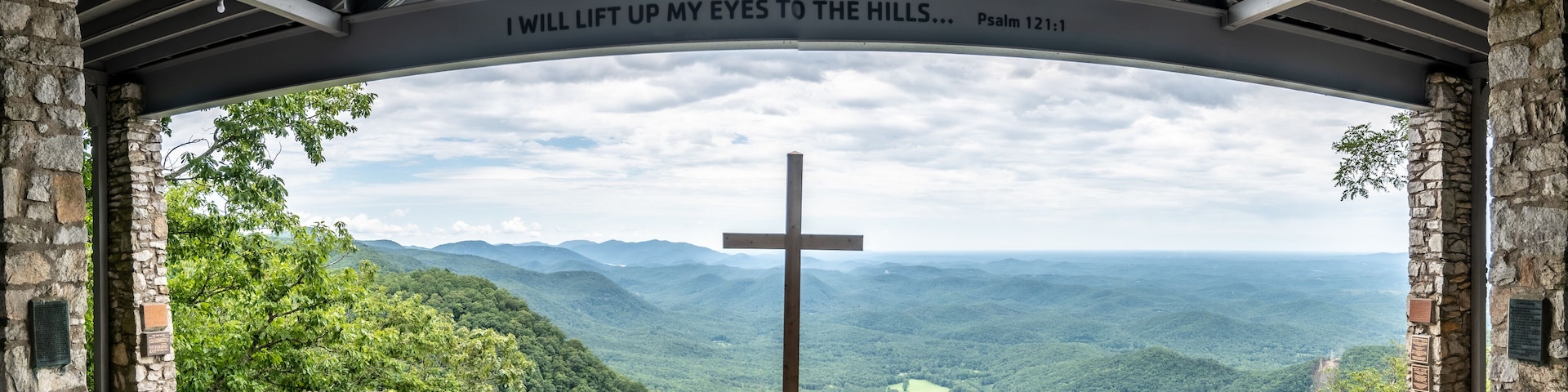 A cross in a stone structure with a view of a mountainous landscape.