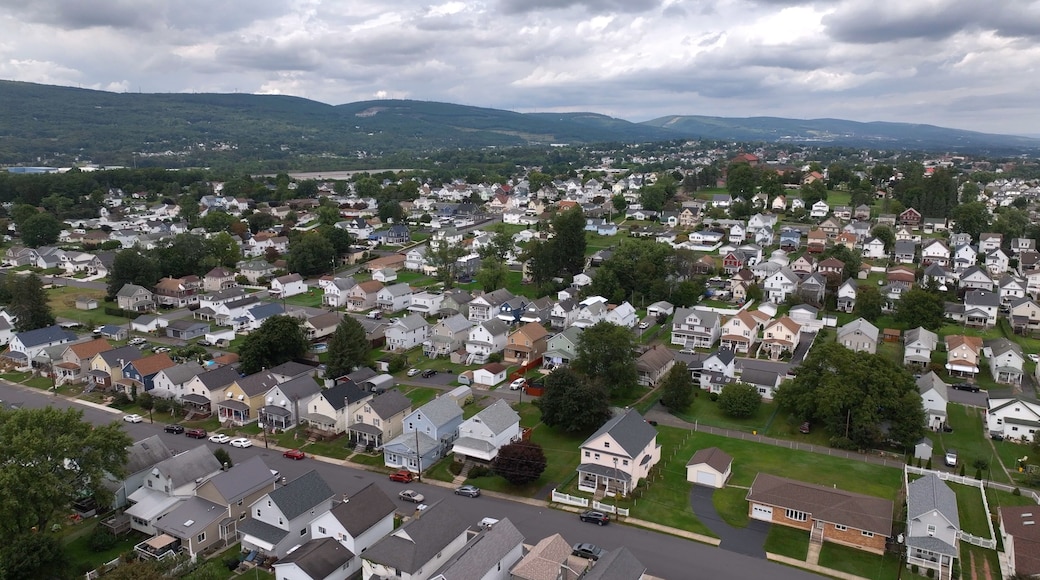A residential area with houses, roads, and green hills in the background.