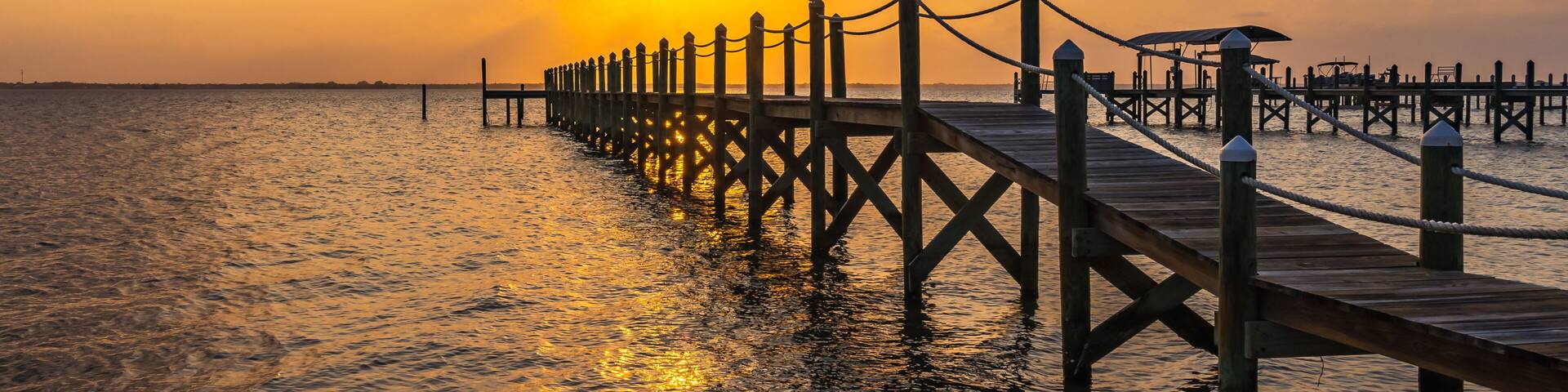 A wooden pier extending into calm waters at sunset.