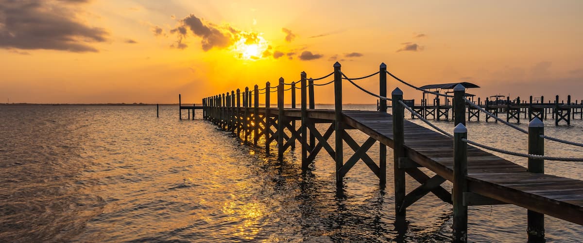 A wooden pier extending into calm waters at sunset.