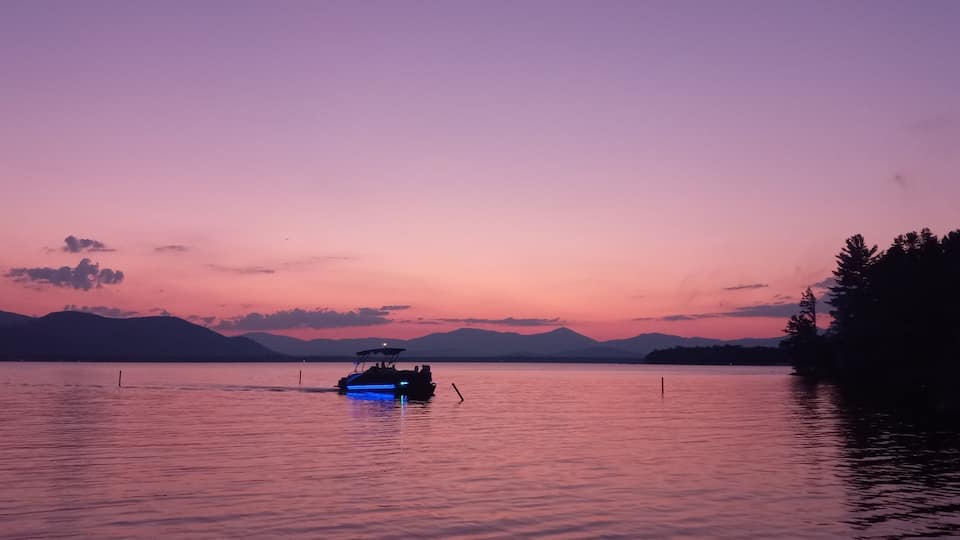 A boat on a calm lake at sunset with mountains in the background.