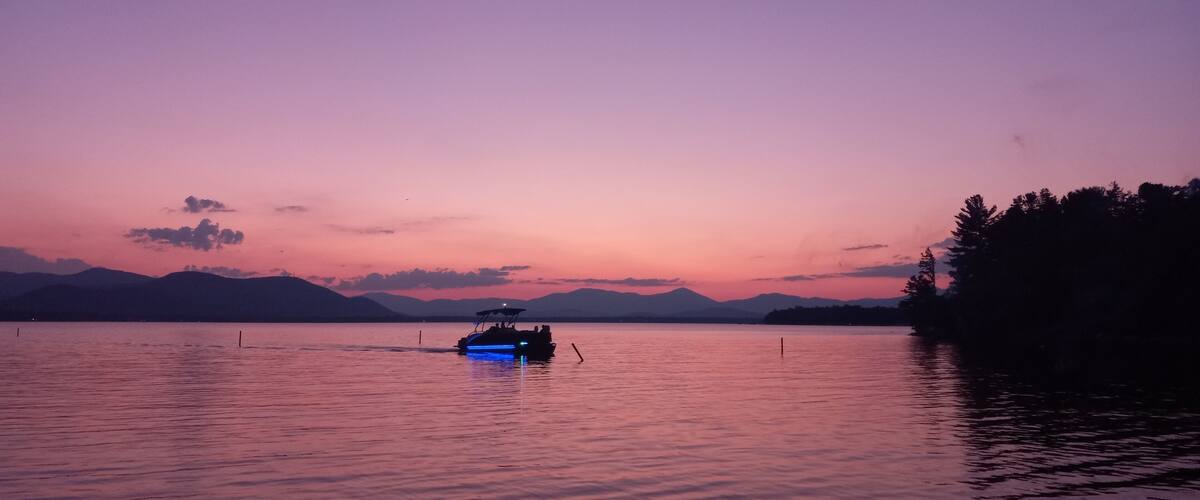 A boat on a calm lake at sunset with mountains in the background.