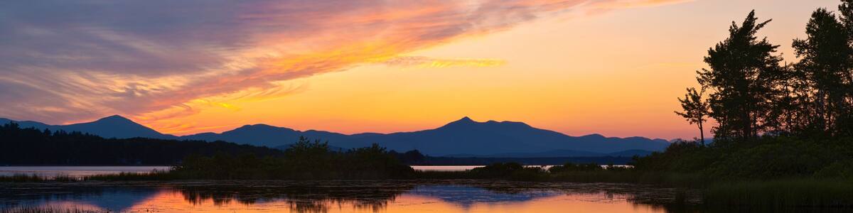 A sunset over a calm lake with mountains in the background.
