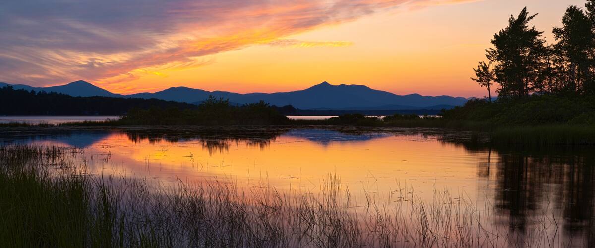 Um pôr do sol sobre um lago calmo, com montanhas ao fundo.