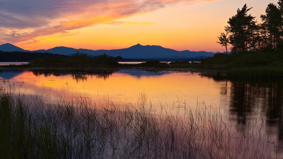 A sunset over a calm lake with mountains in the background.