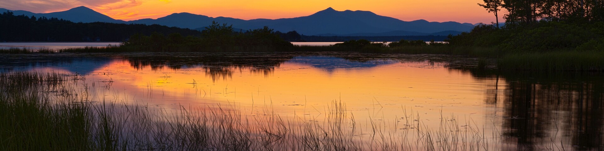 Un atardecer sobre un lago tranquilo con montañas al fondo.