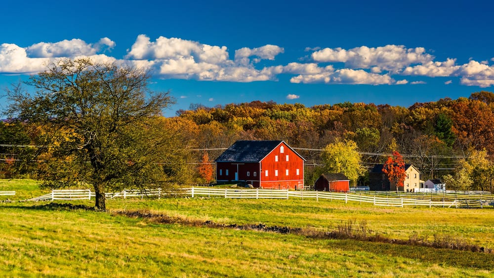 A red barn, white fences, and autumn trees in a rural landscape.