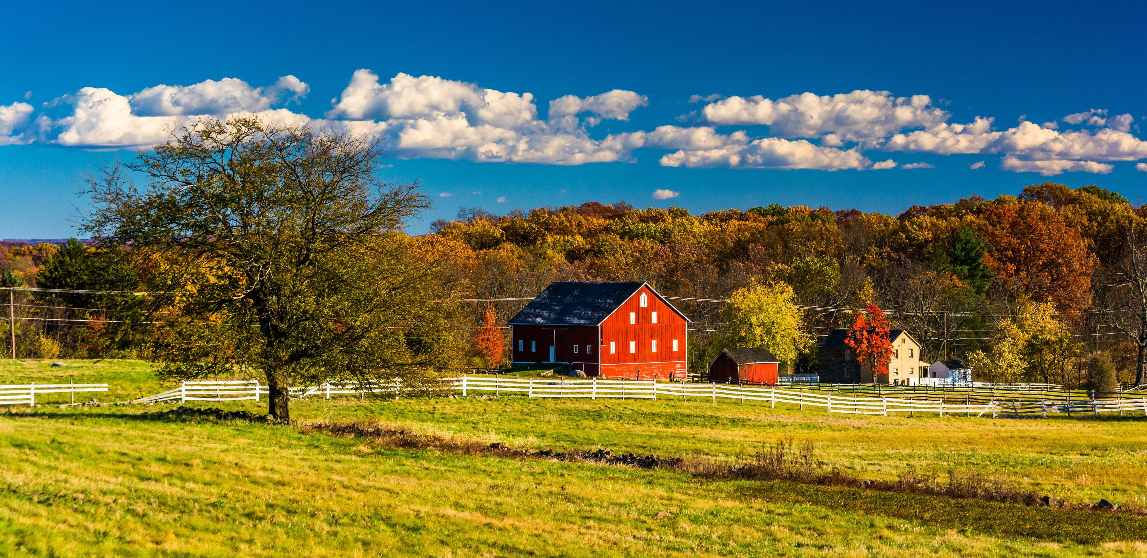 A red barn, white fences, and autumn trees in a rural landscape.