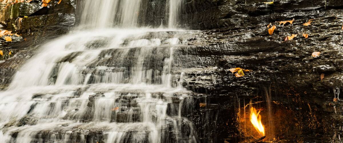 A waterfall cascading over dark rocks with a fire burning at the base.