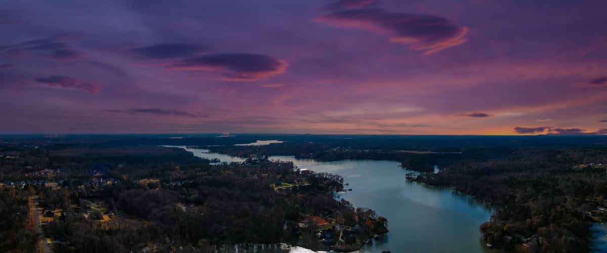 a stunning aerial panoramic shot of the Catawba River surrounded by vast miles of green and autumn colored trees with powerful clouds at sunset in Charlotte North Carolina USA