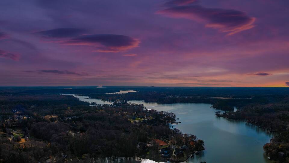 a stunning aerial panoramic shot of the Catawba River surrounded by vast miles of green and autumn colored trees with powerful clouds at sunset in Charlotte North Carolina USA