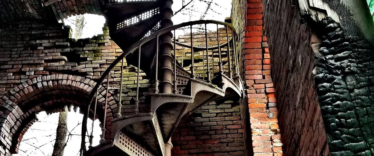 A spiral staircase in an abandoned building with brick walls and a metal railing.