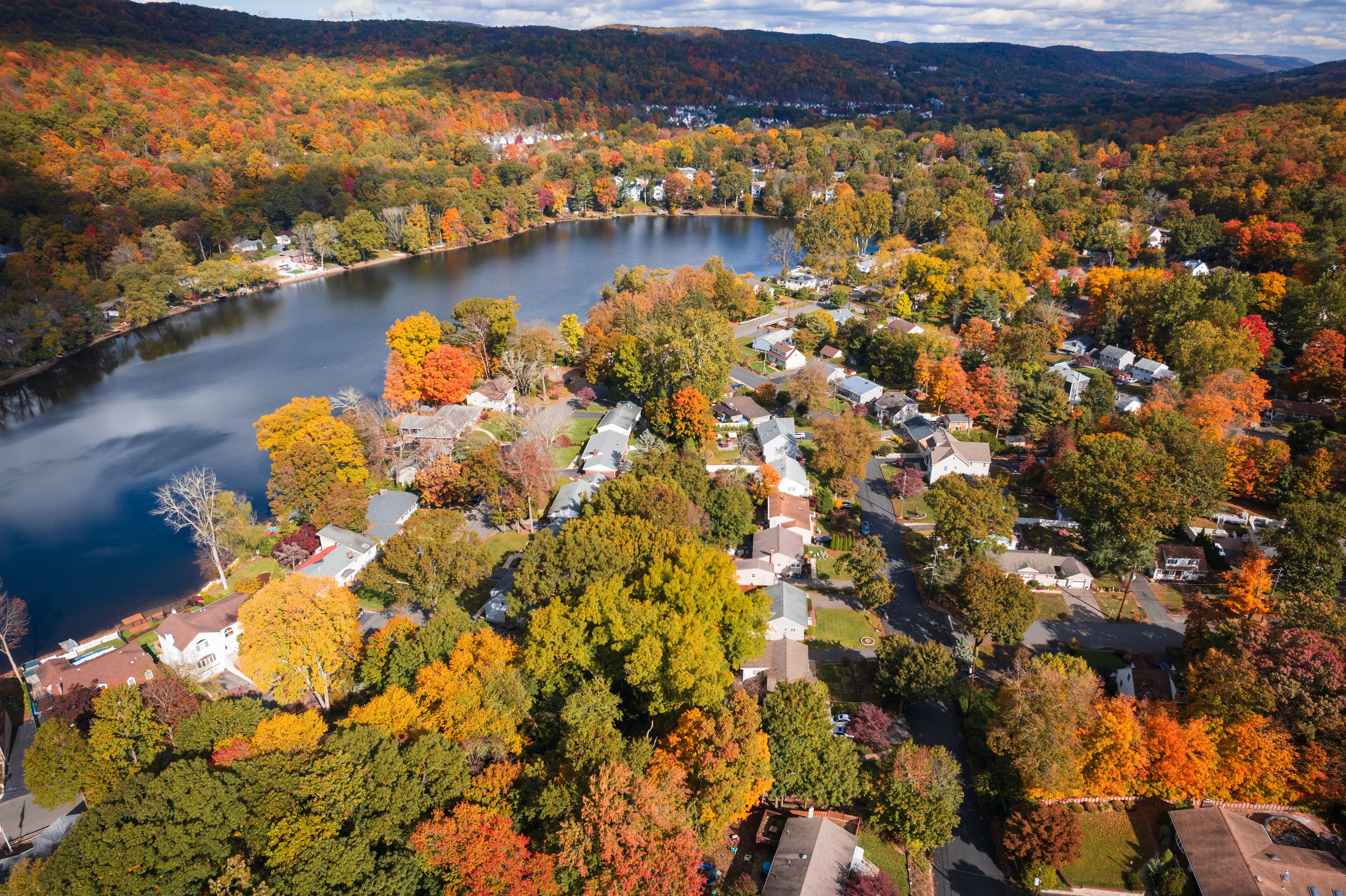 A lake surrounded by autumn-colored trees and residential houses.