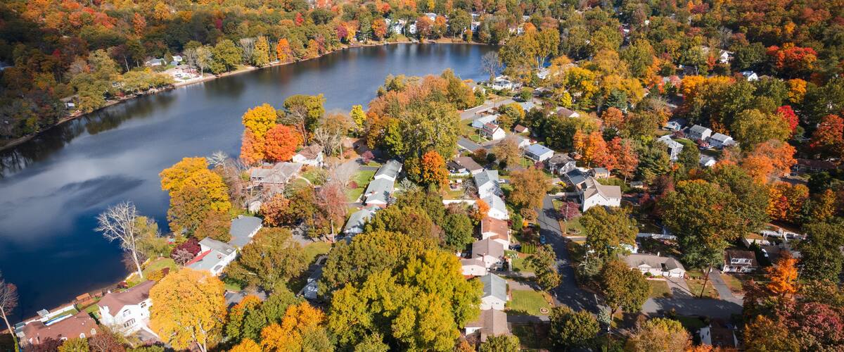 A lake surrounded by autumn-colored trees and residential houses.