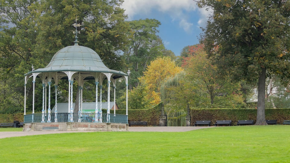 A gazebo in a park with green grass, trees, and benches.
