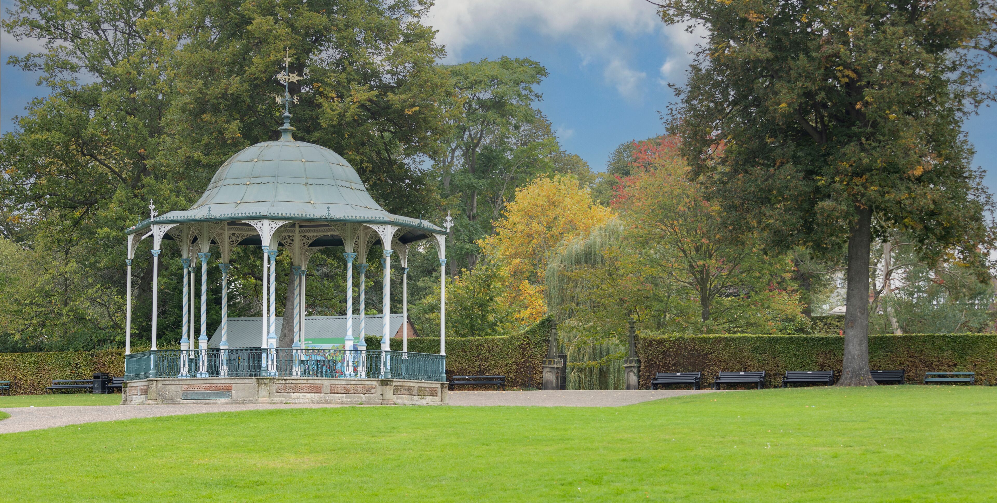 A gazebo in a park with green grass, trees, and benches.