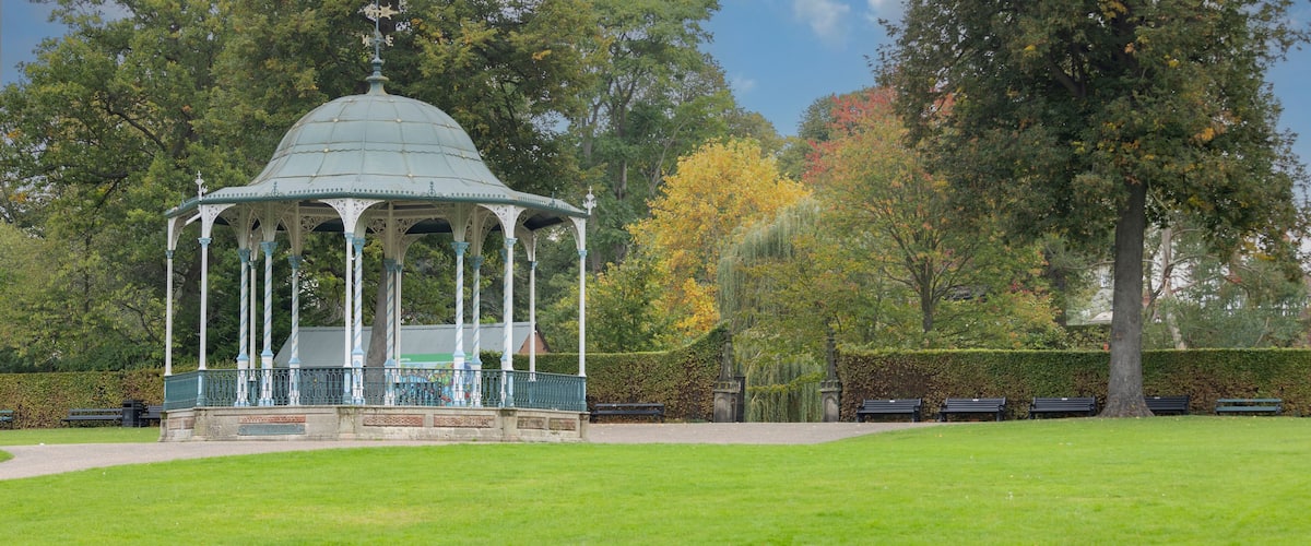 A gazebo in a park with green grass, trees, and benches.
