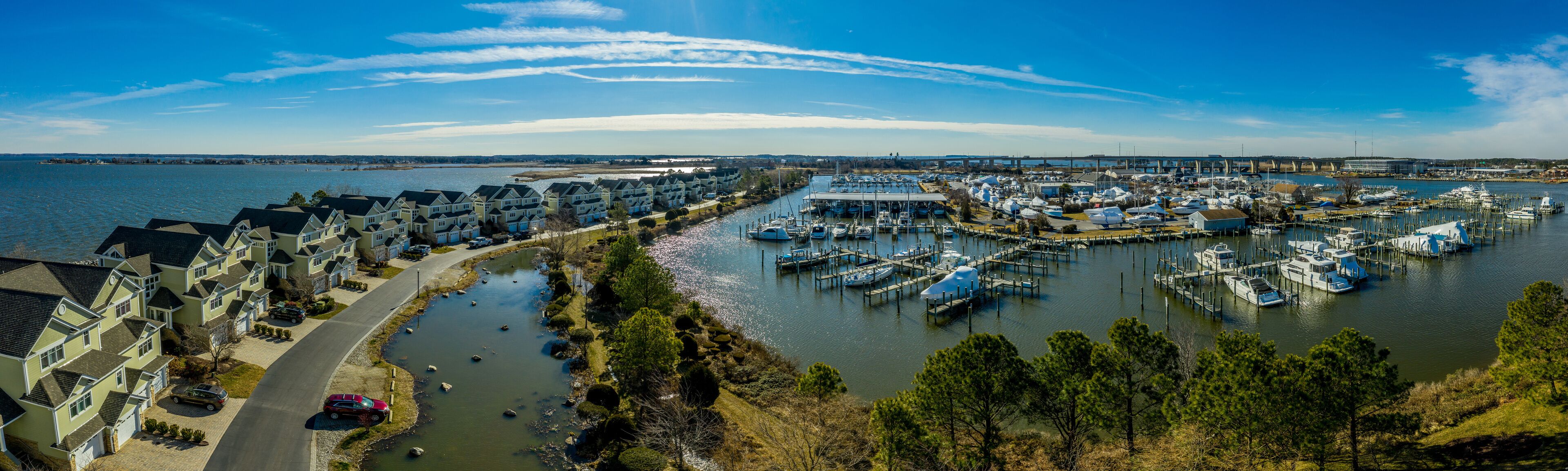A marina with boats docked, a river, and a row of houses along the riverbank.