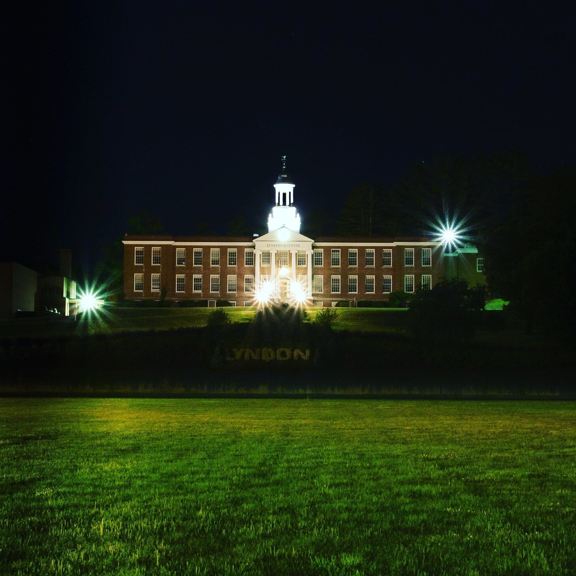 A large brick building with a central tower and two bright lights on either side.