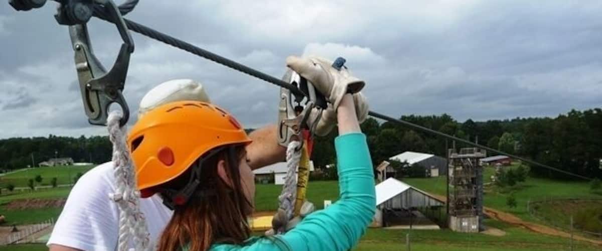 A person in a turquoise shirt and orange helmet preparing to zipline.