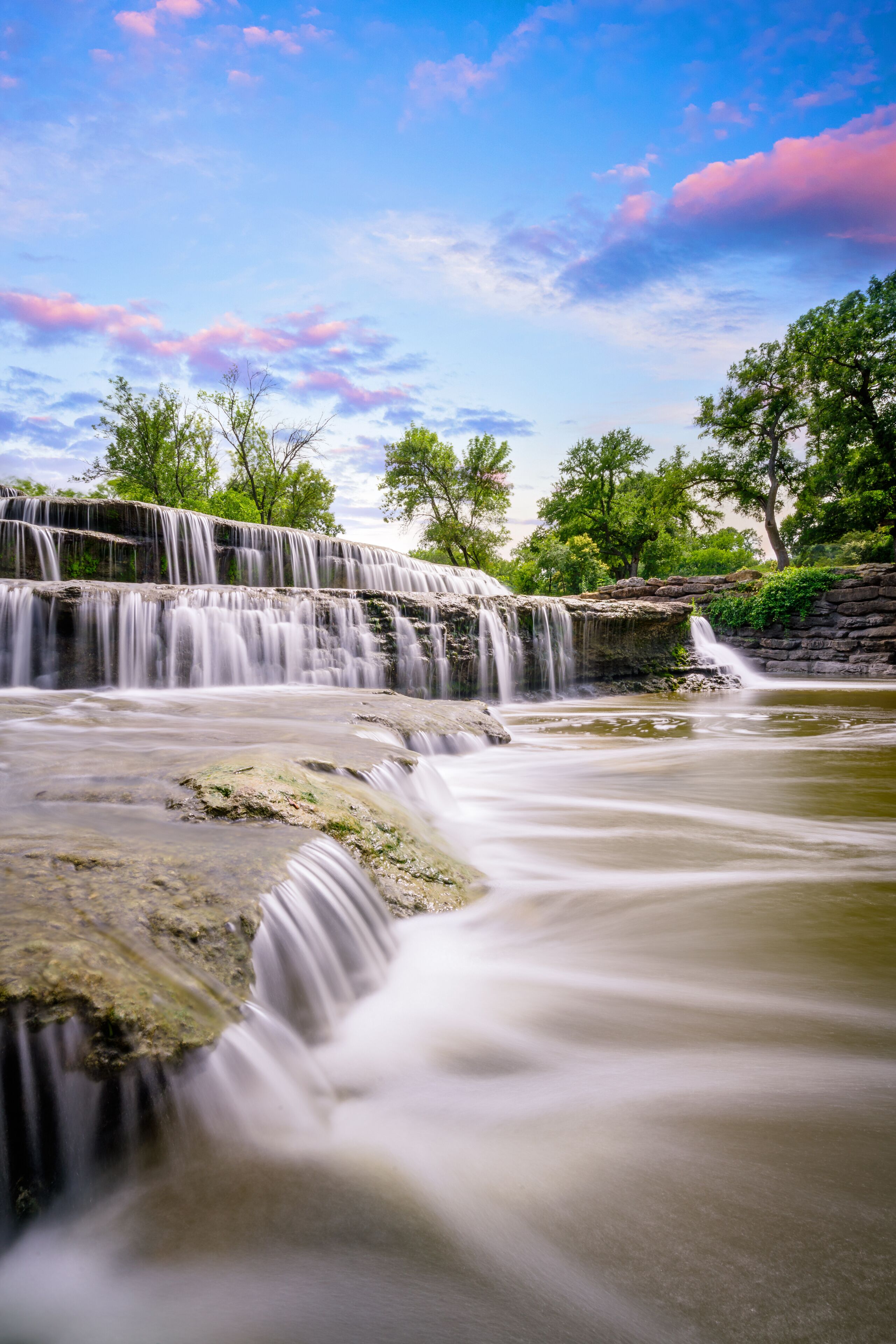 A waterfall cascading over rocks, surrounded by trees and a clear sky.