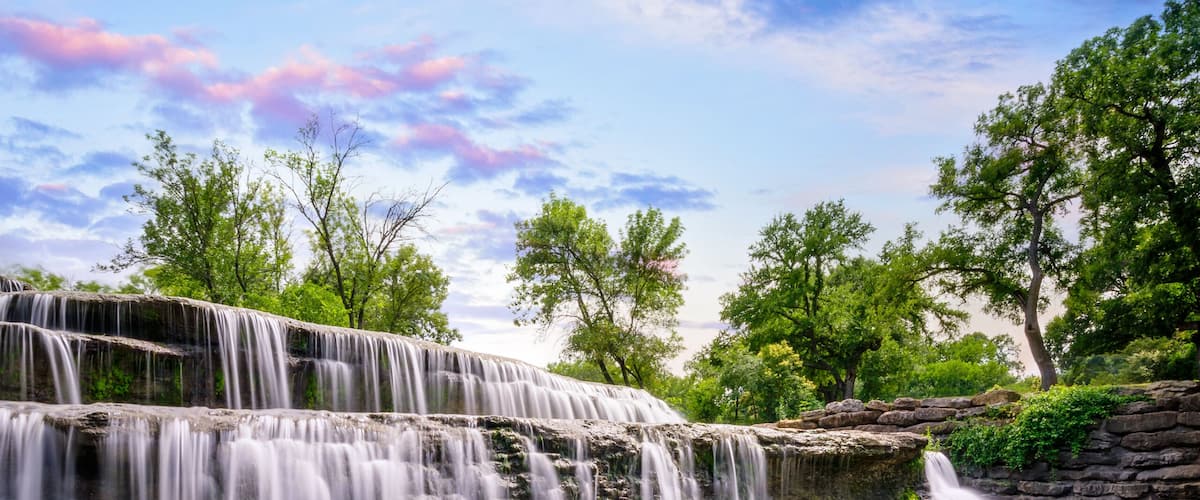 A waterfall cascading over rocks, surrounded by trees and a clear sky.