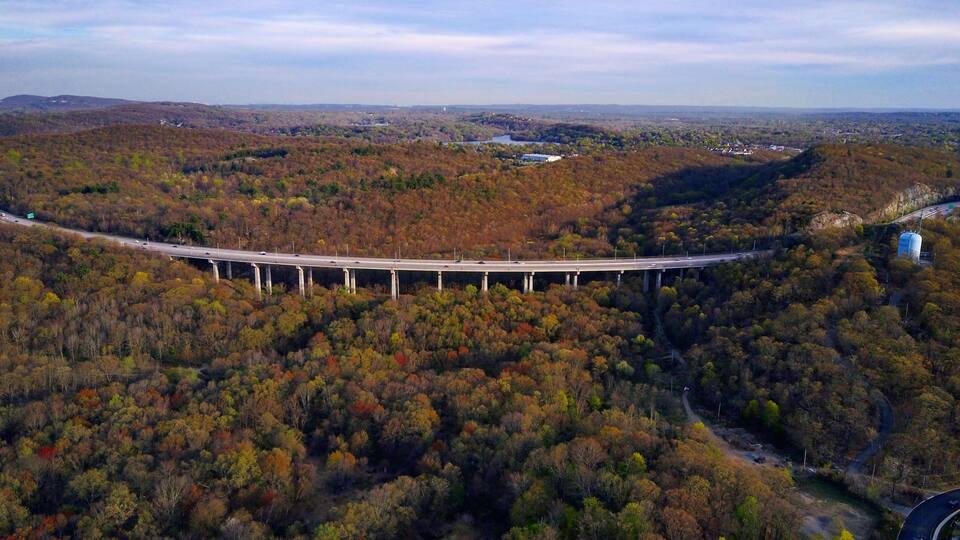 A bridge over a forested valley with autumn foliage.