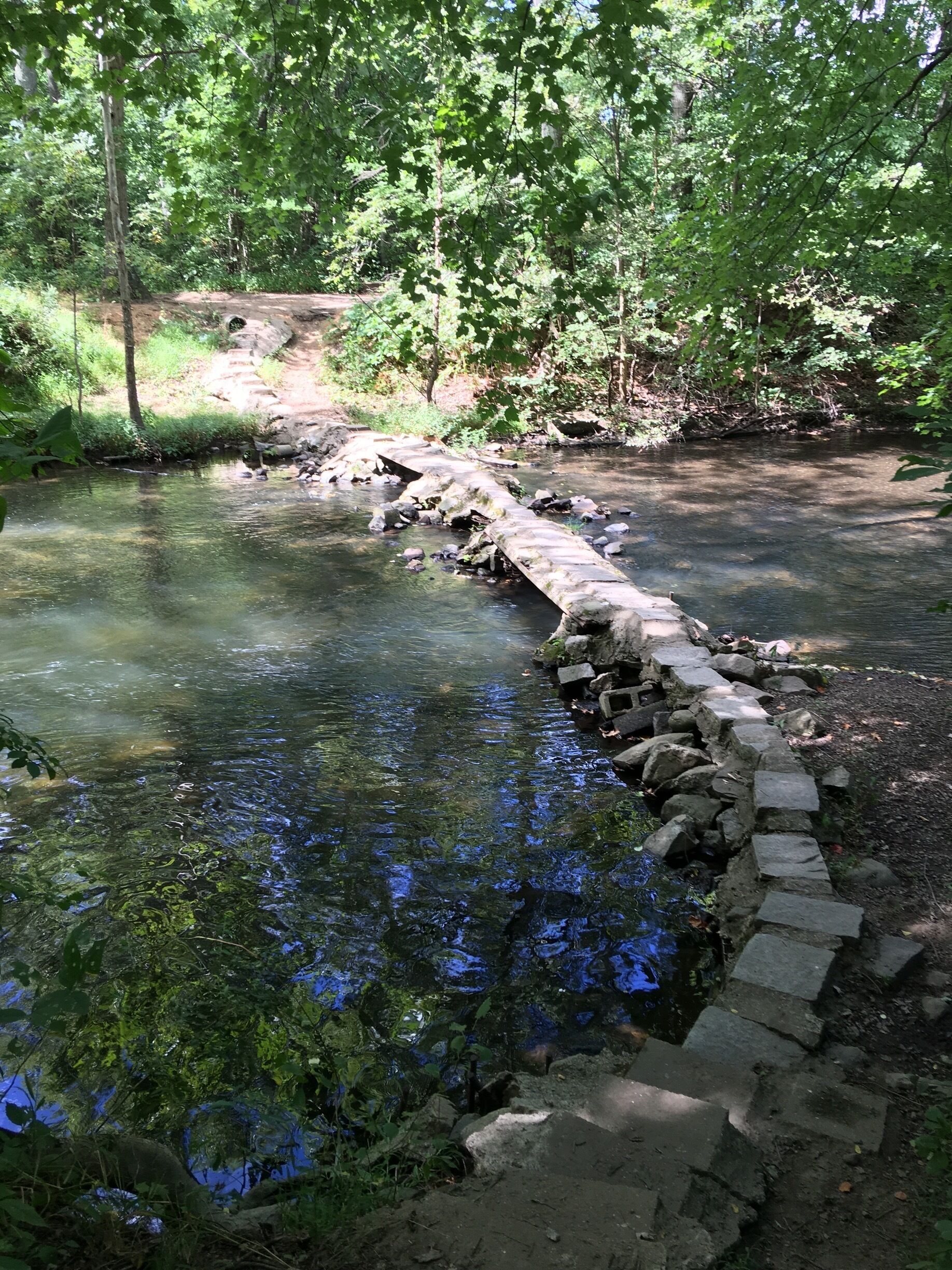 A stone bridge over a clear stream surrounded by dense greenery.