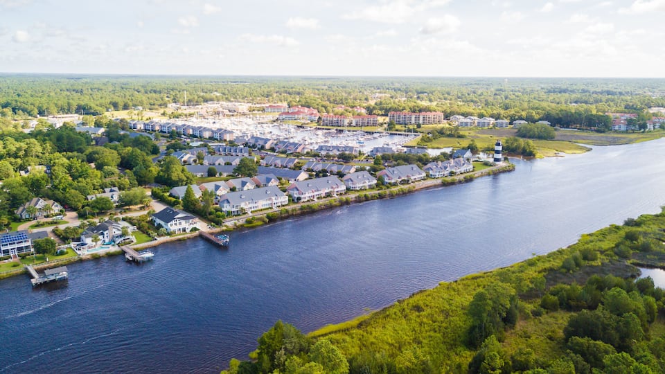 A riverside community with residential buildings, a marina, and a lighthouse.