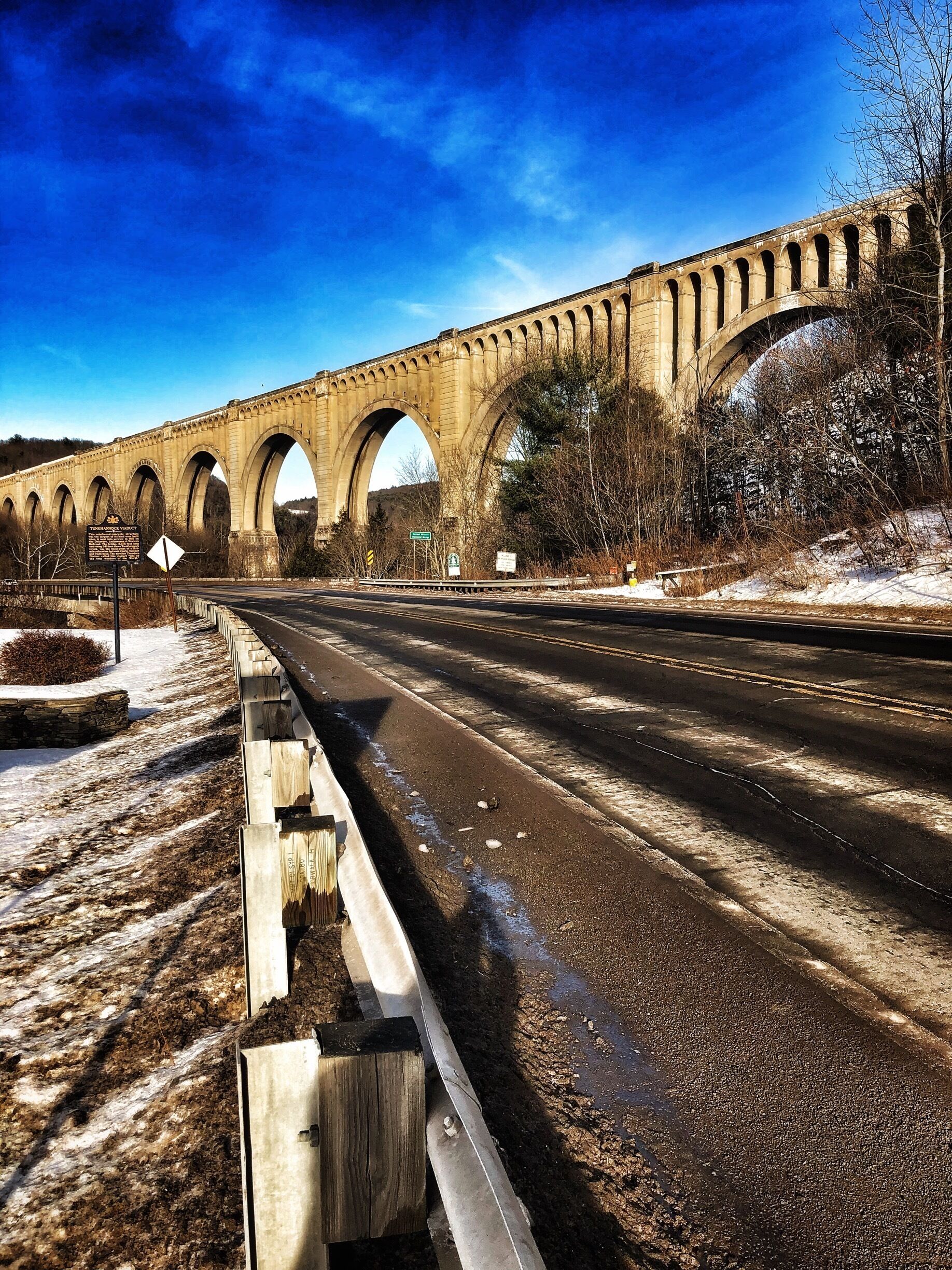 A stone bridge with multiple arches over a road.