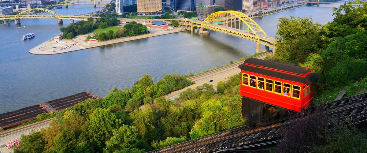 Un paisaje urbano con un puente amarillo destacado sobre un río, rodeado de edificios modernos y abundante vegetación.