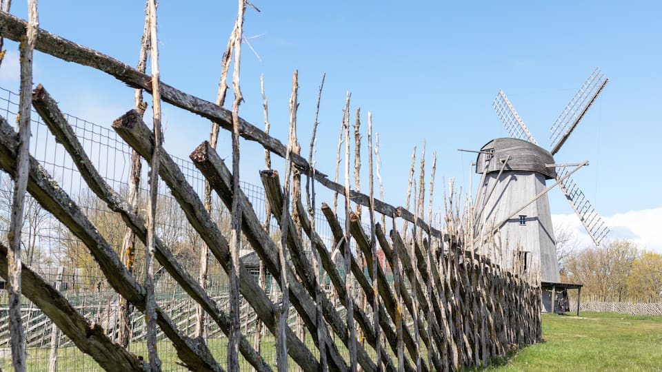 Wooden windmill with a wooden fence on a background of grass and blue sky