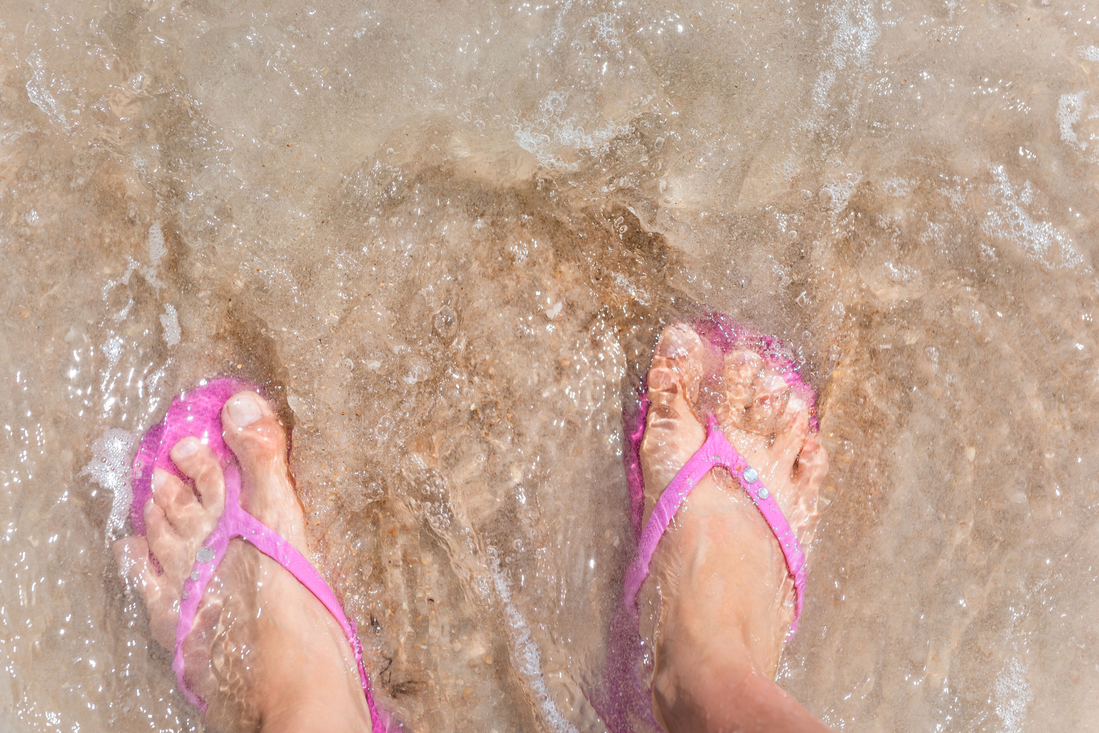 Un par de pies con chanclas rosas sobre aguas poco profundas y transparentes.