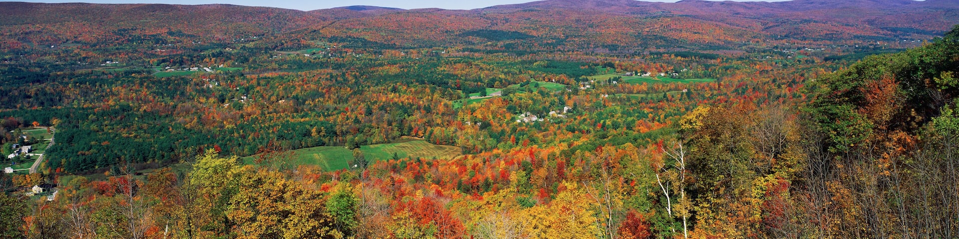 A mountainous landscape with autumn foliage, green fields, and scattered houses.
