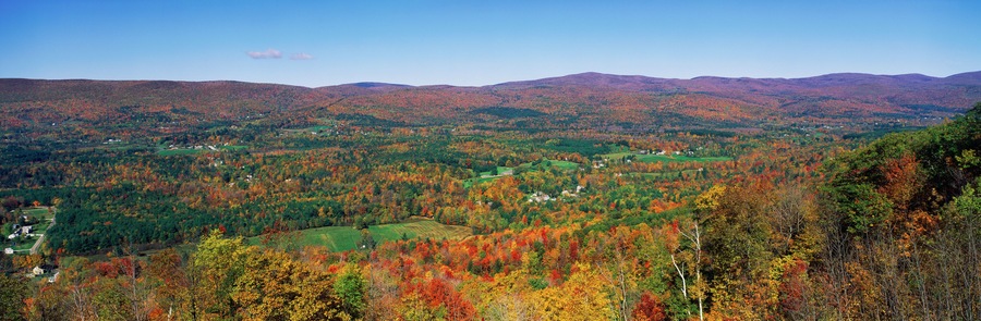 A mountainous landscape with autumn foliage, green fields, and scattered houses.