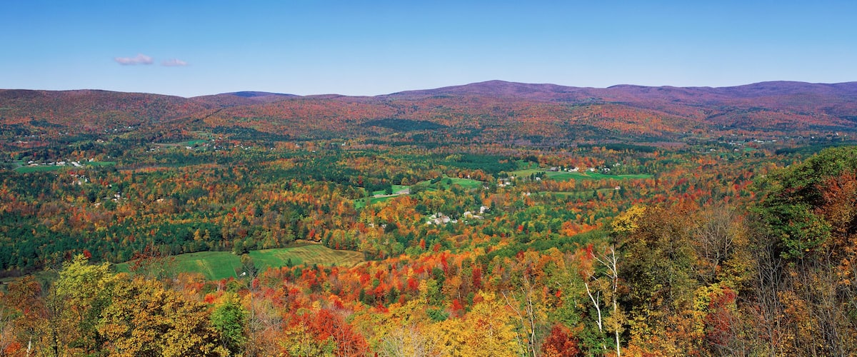 A mountainous landscape with autumn foliage, green fields, and scattered houses.