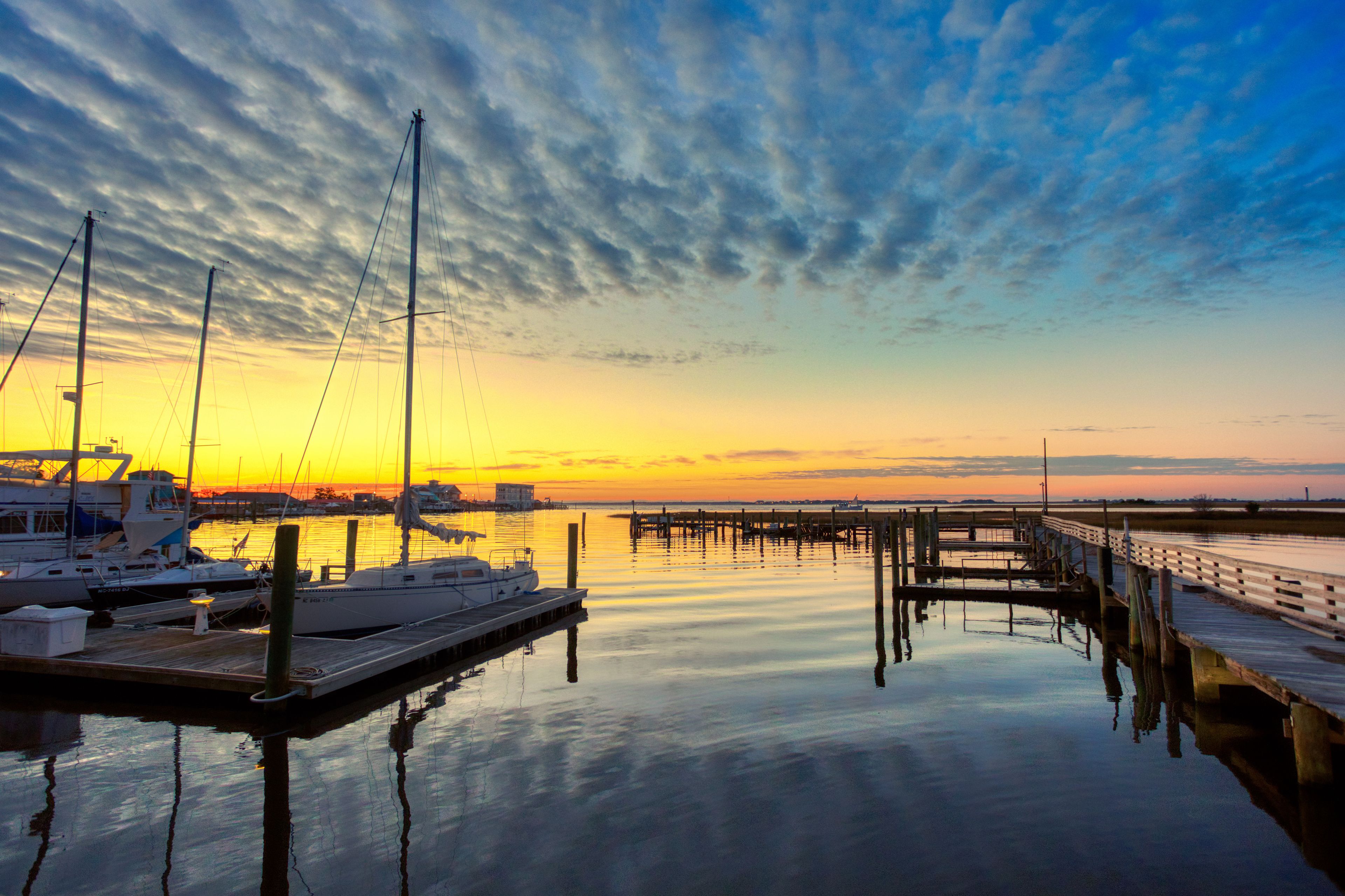 A marina with boats docked, a wooden pier, and a sunset over the water.