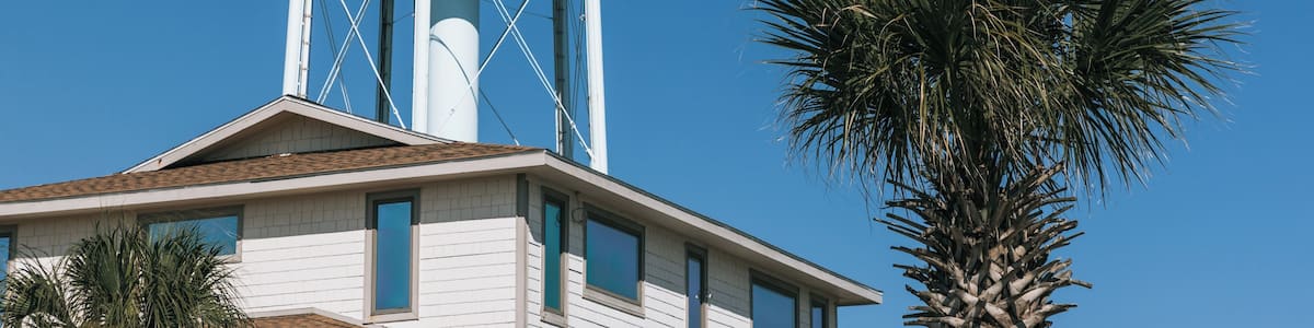 A water tower with 'WELCOME TO HOLDEN BEACH' written on it, a palm tree, and a building with a sloped roof.