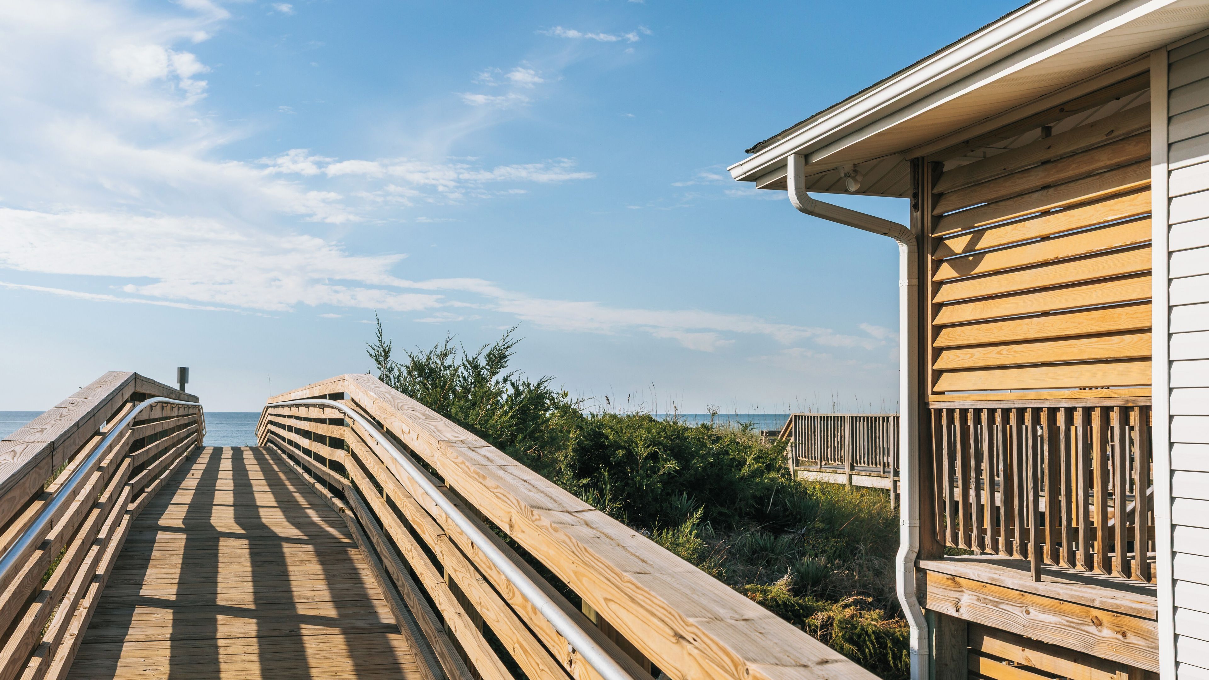 A wooden boardwalk leading to a beach, with a wooden building on the right.