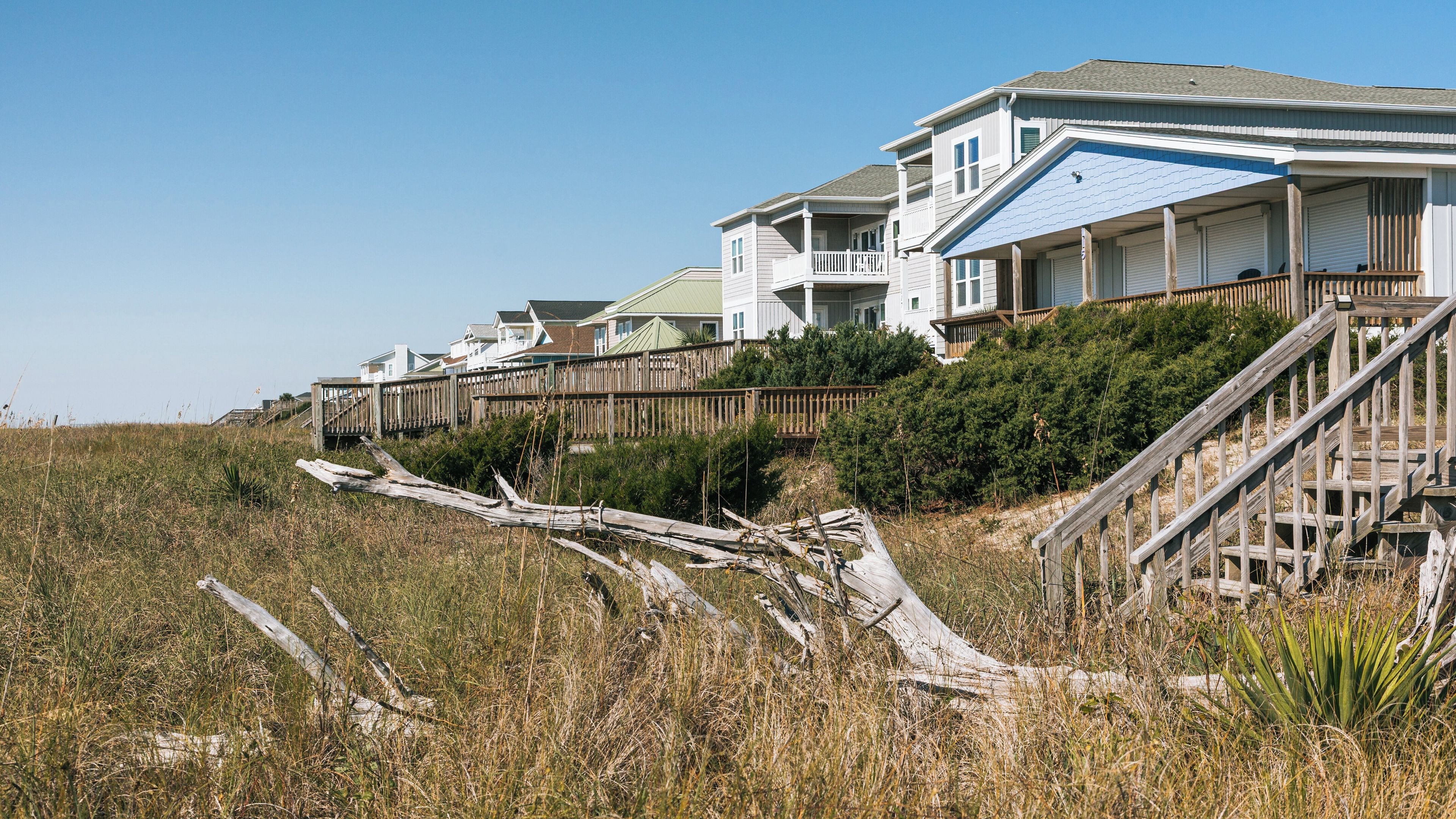 A coastal residential area with houses, a wooden staircase, and a fallen tree.